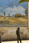 Eritrea - Asmara: soldier in front of a mural with a village scene - photo by E.Petitalot
