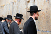 Jerusalem, Israel: line of Ortodox Jews in their traditional black clothing praying at the Wailing wall - as no mortar was used in the masonry, the lower joints between the chalky, yellow-white ashlar blocks have been stuffed with bits of paper containing prayers / Western Wall / the Kotel - muro das lamentaes - Mur des Lamentations - Klagemauer - photo by M.Torres