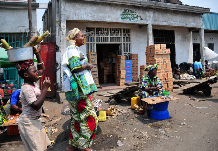 congo-dr5: Goma, Nord-Kivu, Democratic Republic of the Congo: street scene - commerce - woman in traditional clothes and girl with sugar cane - Kerrygold logo - piles of Rwenzori and Riham power boxes - photo by M.Torres - (c) Travel-Images.com - Stock Photography agency - Image Bank