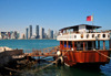Doha, Qatar: old boat with Qatari flag in the Dhow harbour - West Bay skyline from the south side of Doha Bay - photo by M.Torres